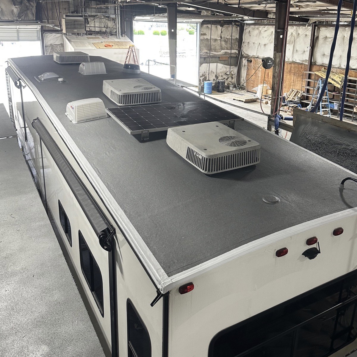 The same RV after the RynoRoof polyurea membrane was sprayed on: one continuous grey surface running the full length of the roof and wrapping the edges, with the vents, air conditioners and solar panel reinstalled.